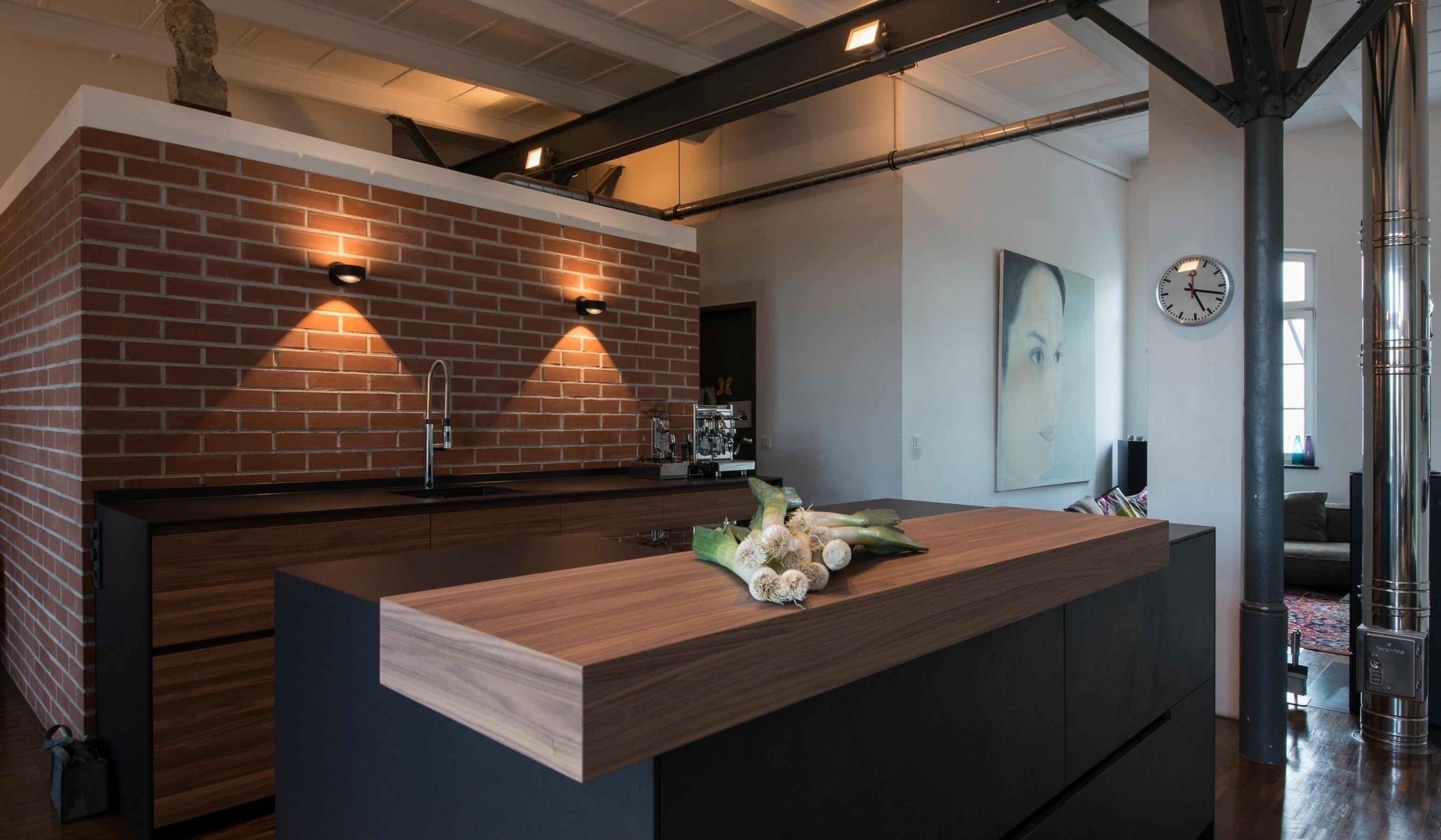Moderne Loftküche mit Backsteinwand, Holzinsel und großem Fenster im Hintergrund.