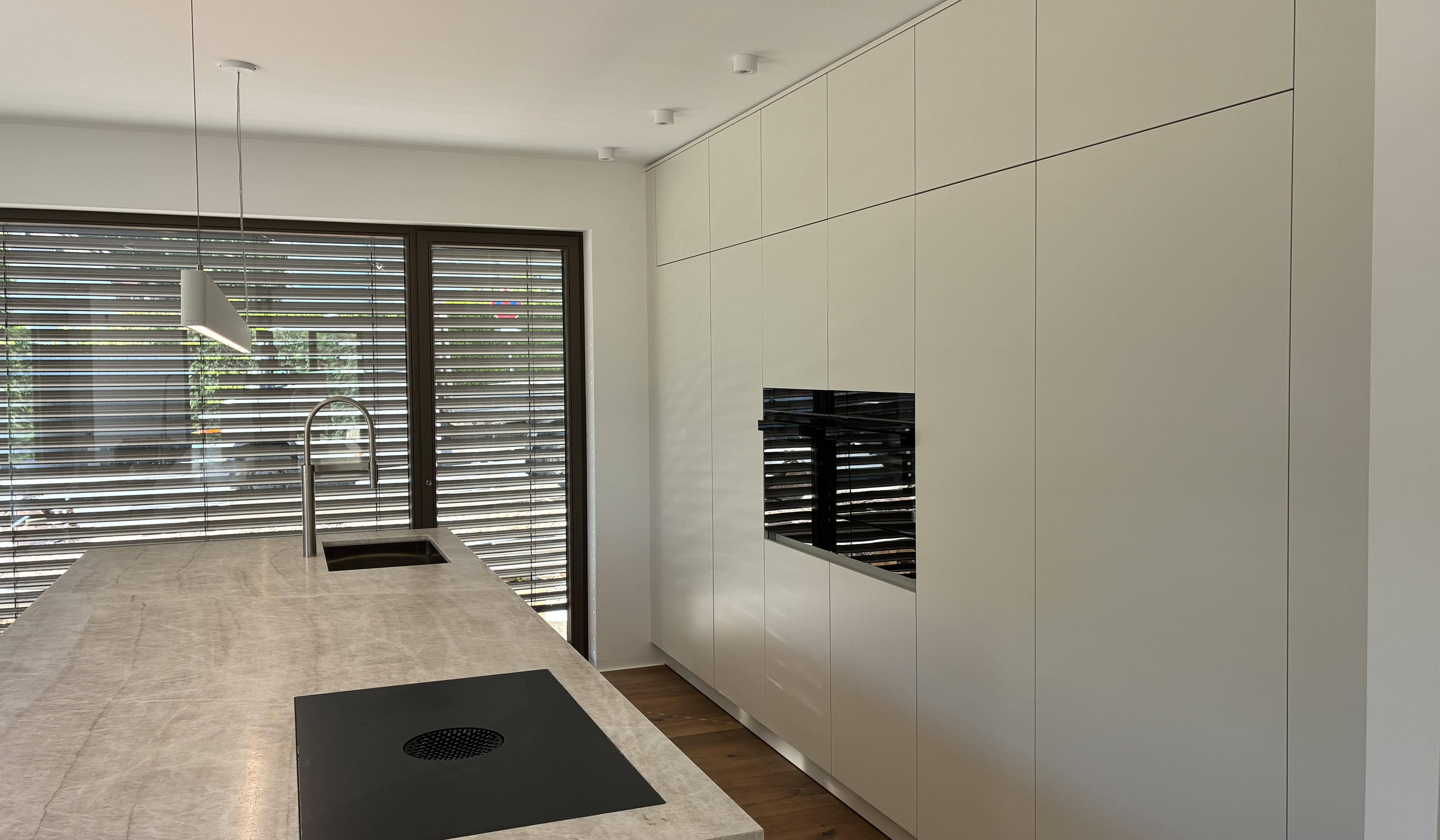 Moderne, helle Küche mit Kochinsel, Einbaugeräten und großen Fensterjalousien.