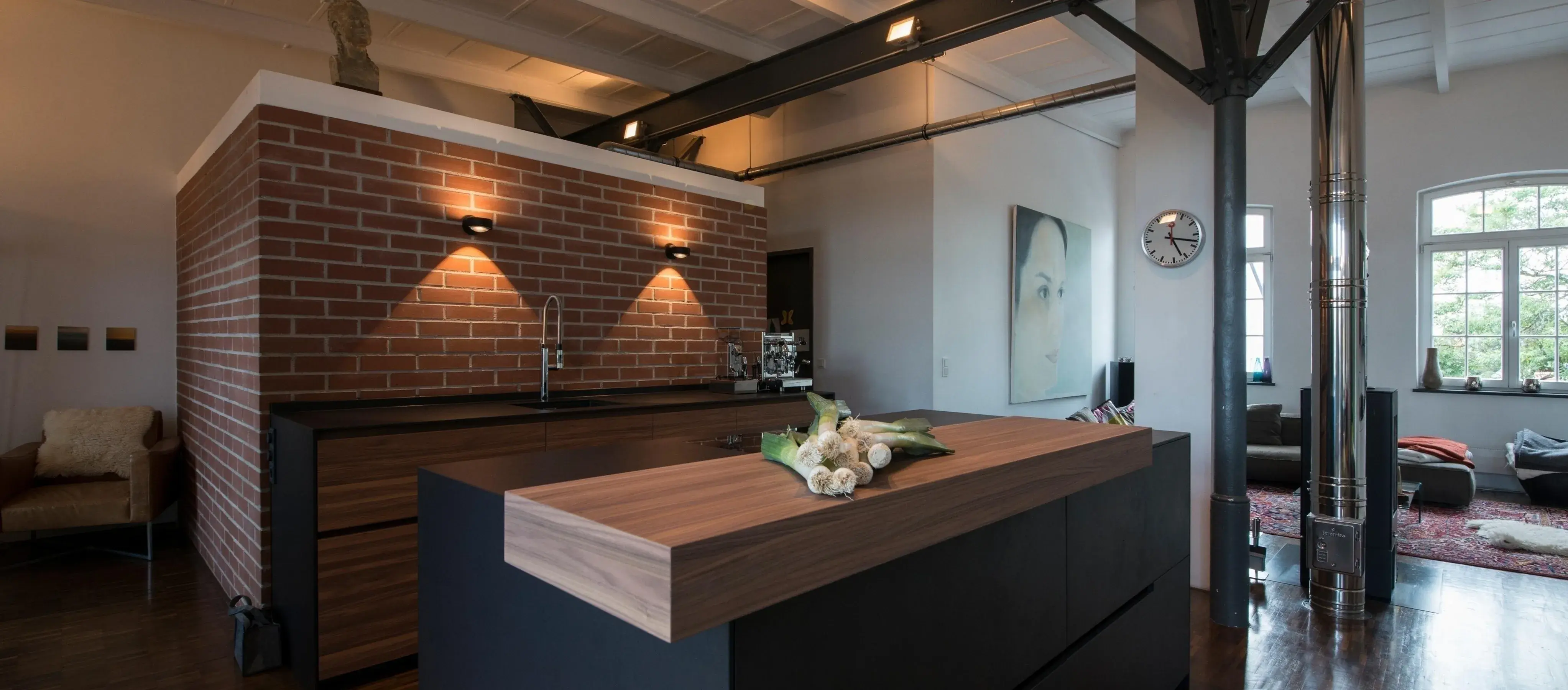 Moderne Loftküche mit Backsteinwand, Holzinsel und großem Fenster im Hintergrund.