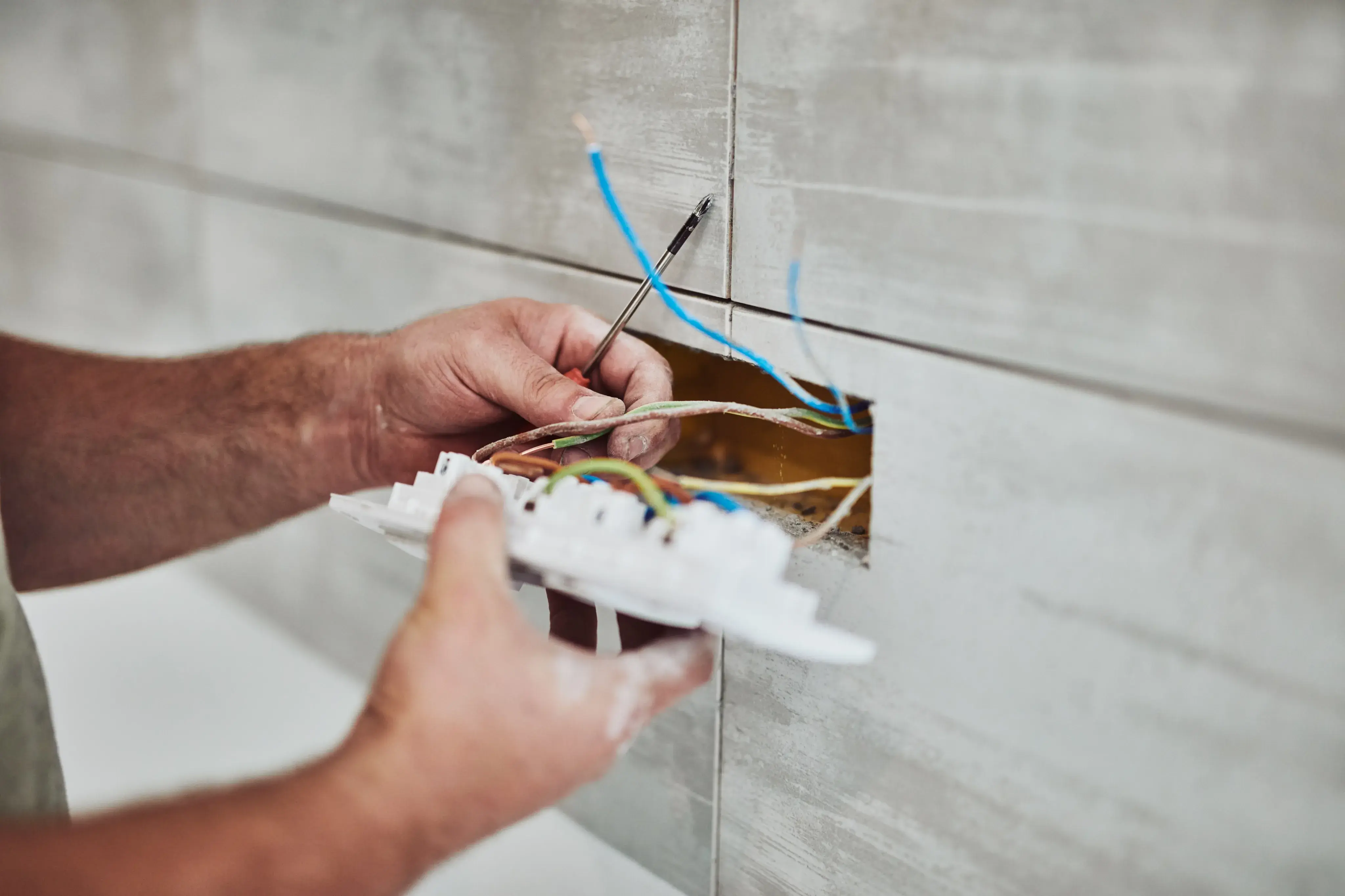 Elektriker installiert Steckdose in gefliester Wand.