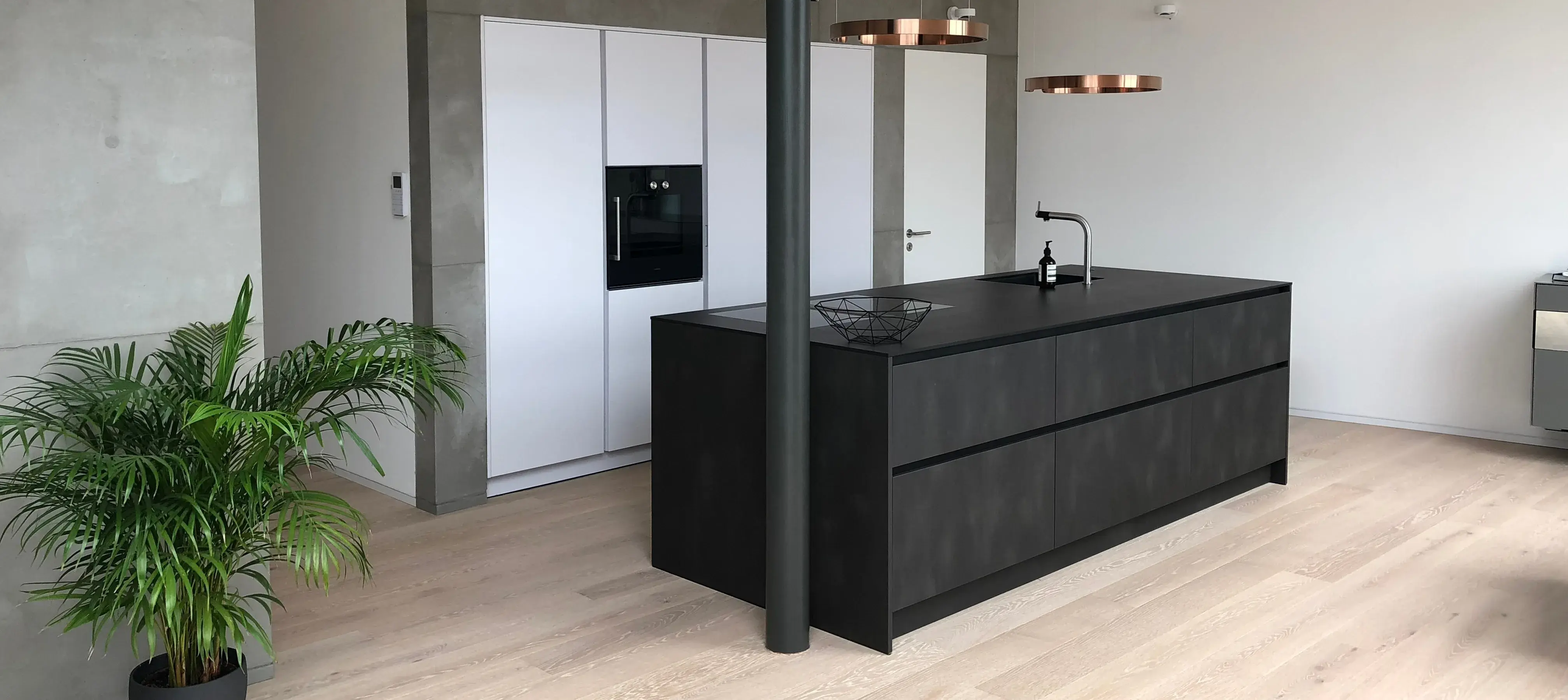 Moderne Küche mit dunkler Kochinsel, Holzfußboden und einer grünen Zimmerpflanze.