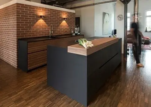 Moderne Küche mit dunkler Kochinsel, Holzdetails und Ziegelwand im Hintergrund.