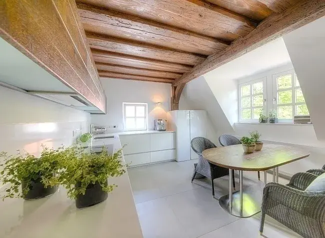 Helle Küche mit Holzbalkendecke, Esstisch, Pflanzen und großen Fenstern