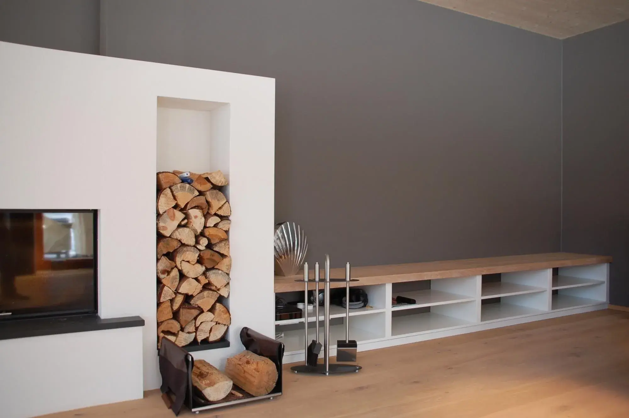 Modernes Wohnzimmer mit Kamin, gestapeltem Feuerholz und grauer Wand.