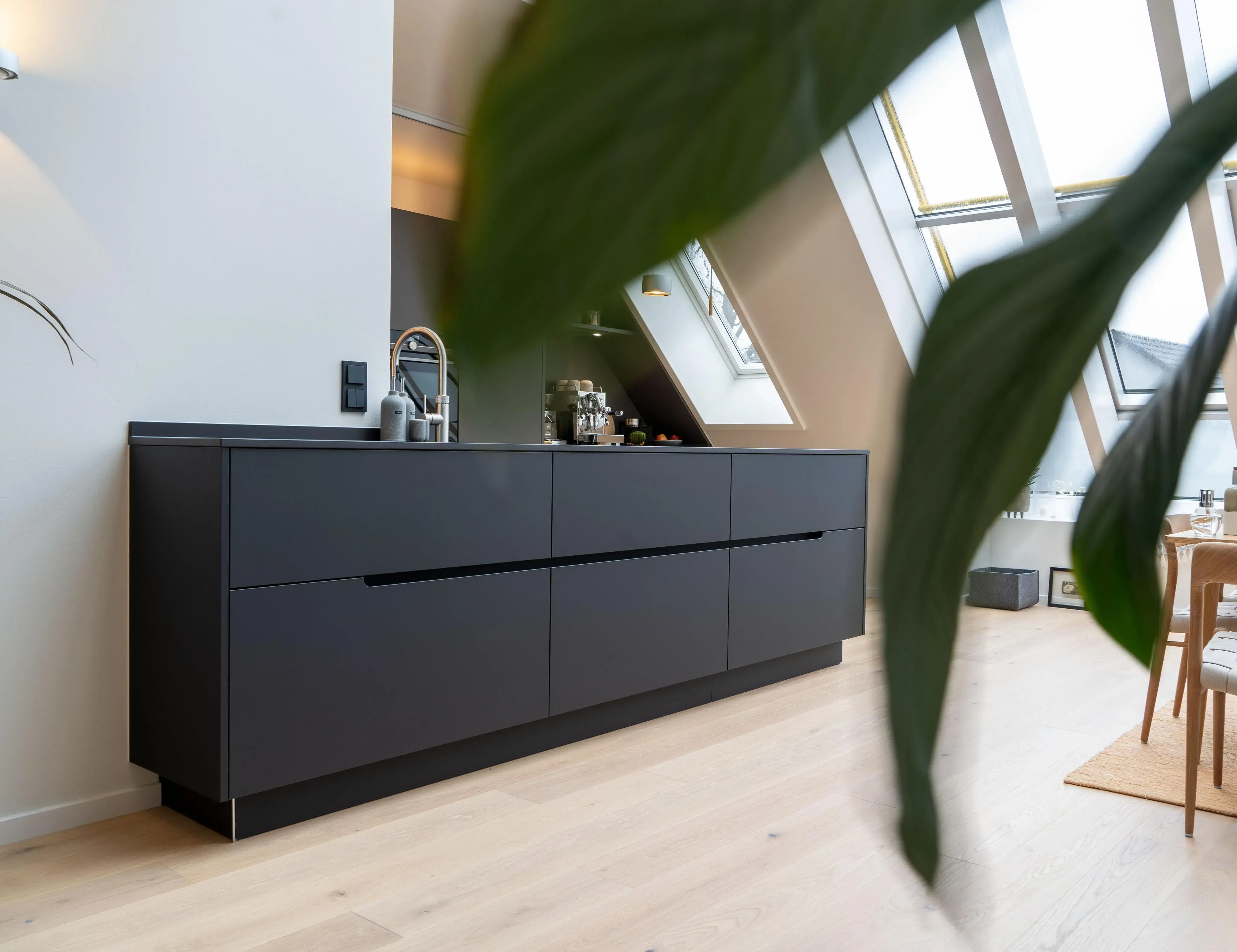 Moderne schwarze Küchenzeile mit großem Fenster und unscharfem Blatt im Vordergrund.
