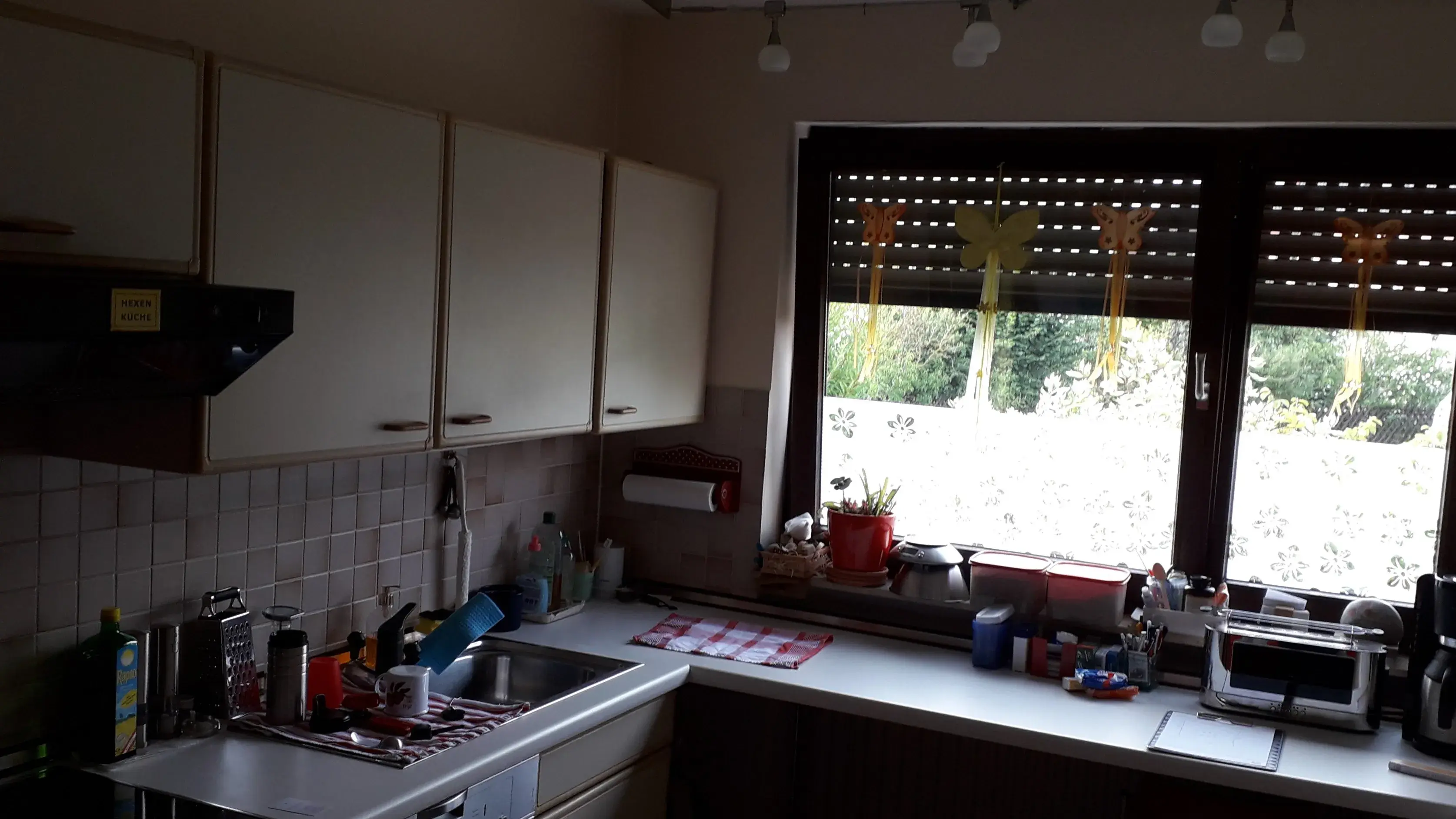 Helle Küche mit großem Fenster, Spüle, Geschirr und Küchengeräten auf der Arbeitsfläche.