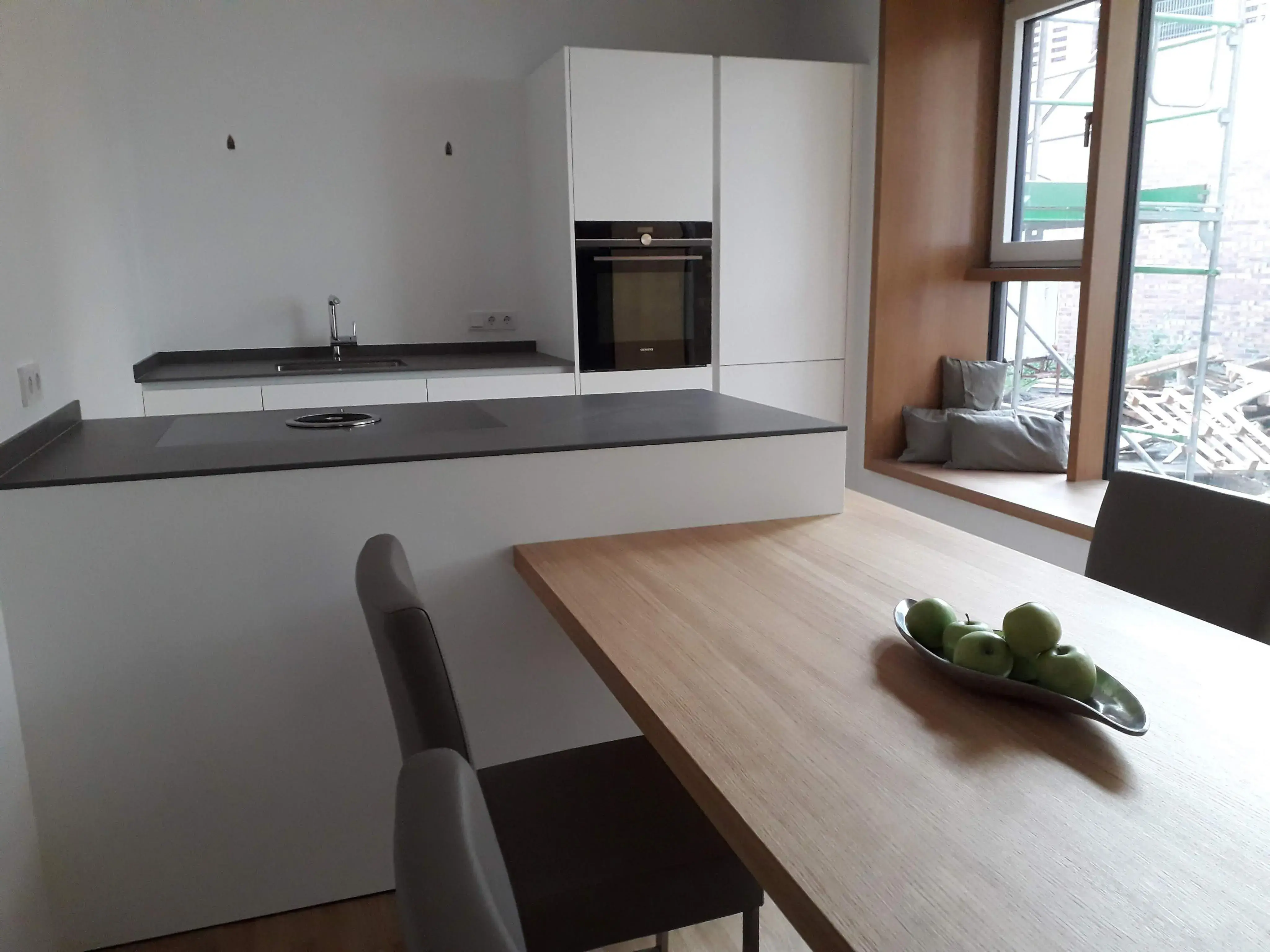 Moderne Küche mit Holztisch, Obstschale und großem Fenster.