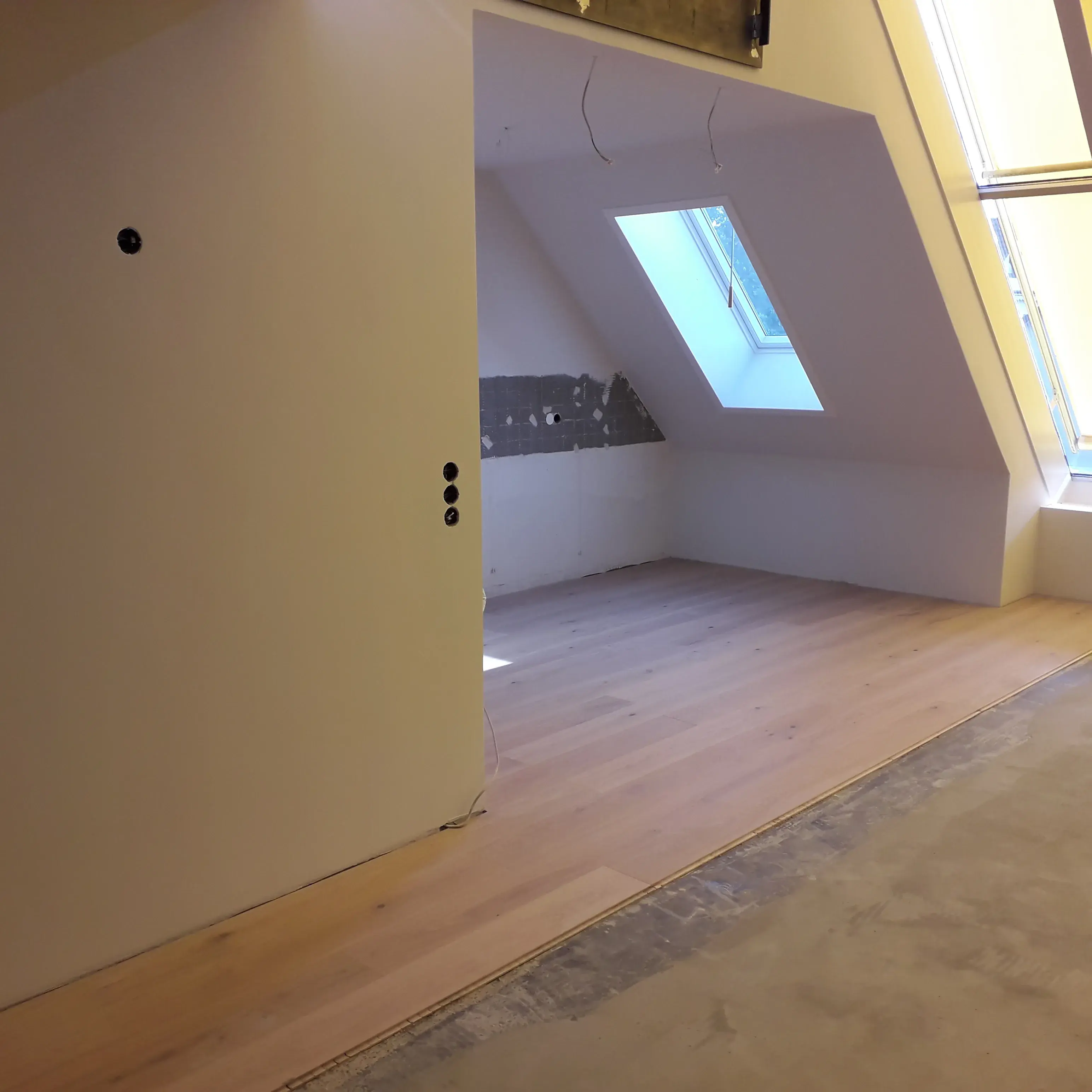 Dachgeschosszimmer mit Holzfußboden und Dachfenster, teils noch im Rohbau.