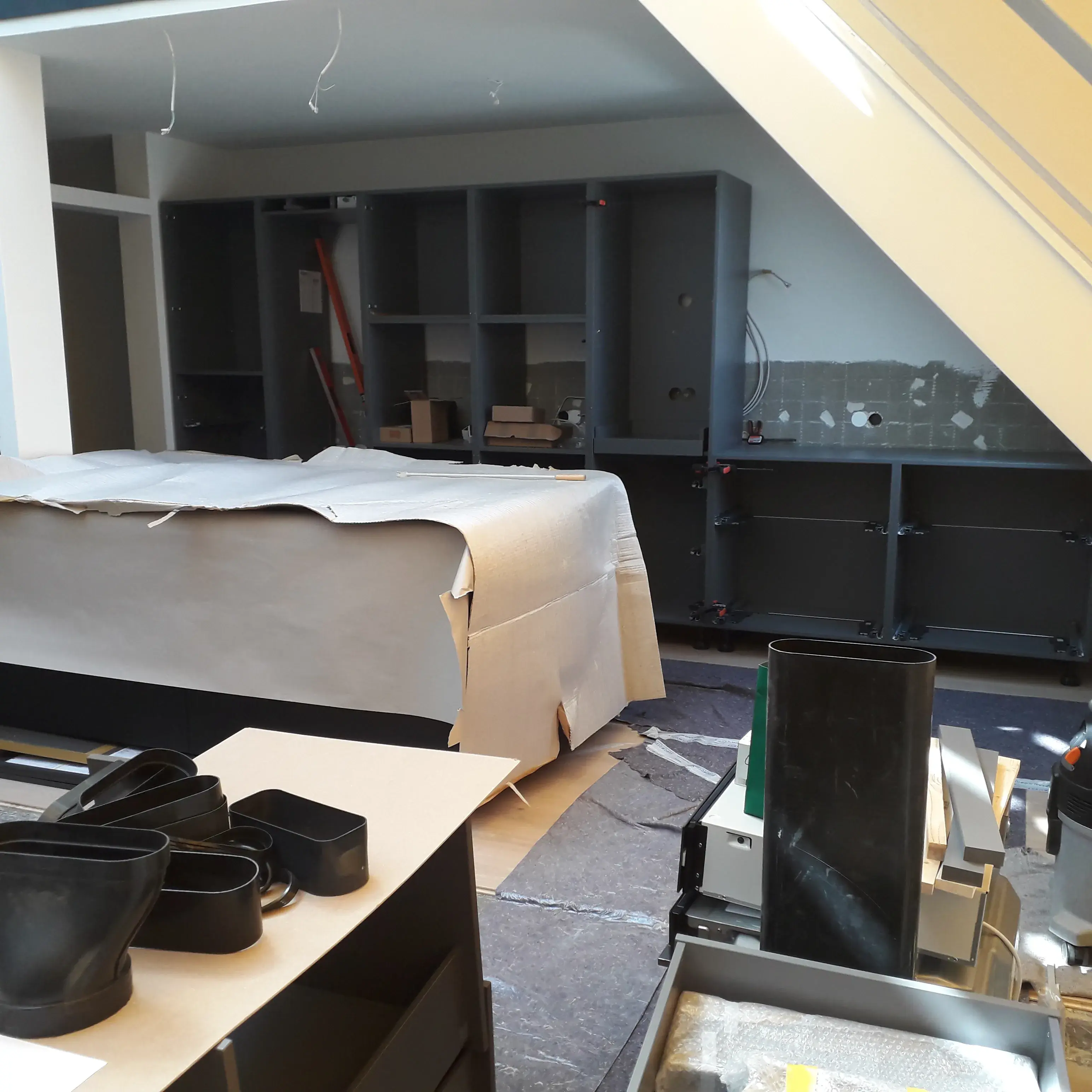 Küche im Aufbau mit abgedeckten Möbeln und Werkzeugen unter einer Treppe.