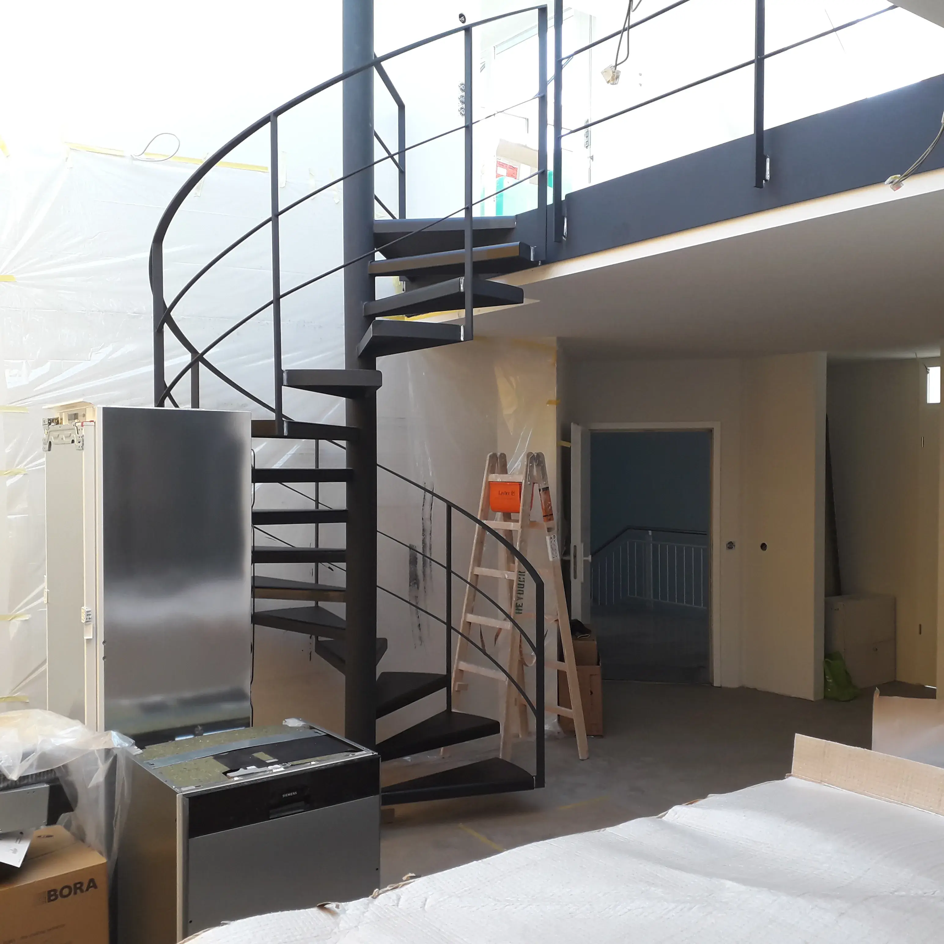Schwarze Wendeltreppe in modernem, teils eingerichteten Raum mit Kartons und Leiter.
