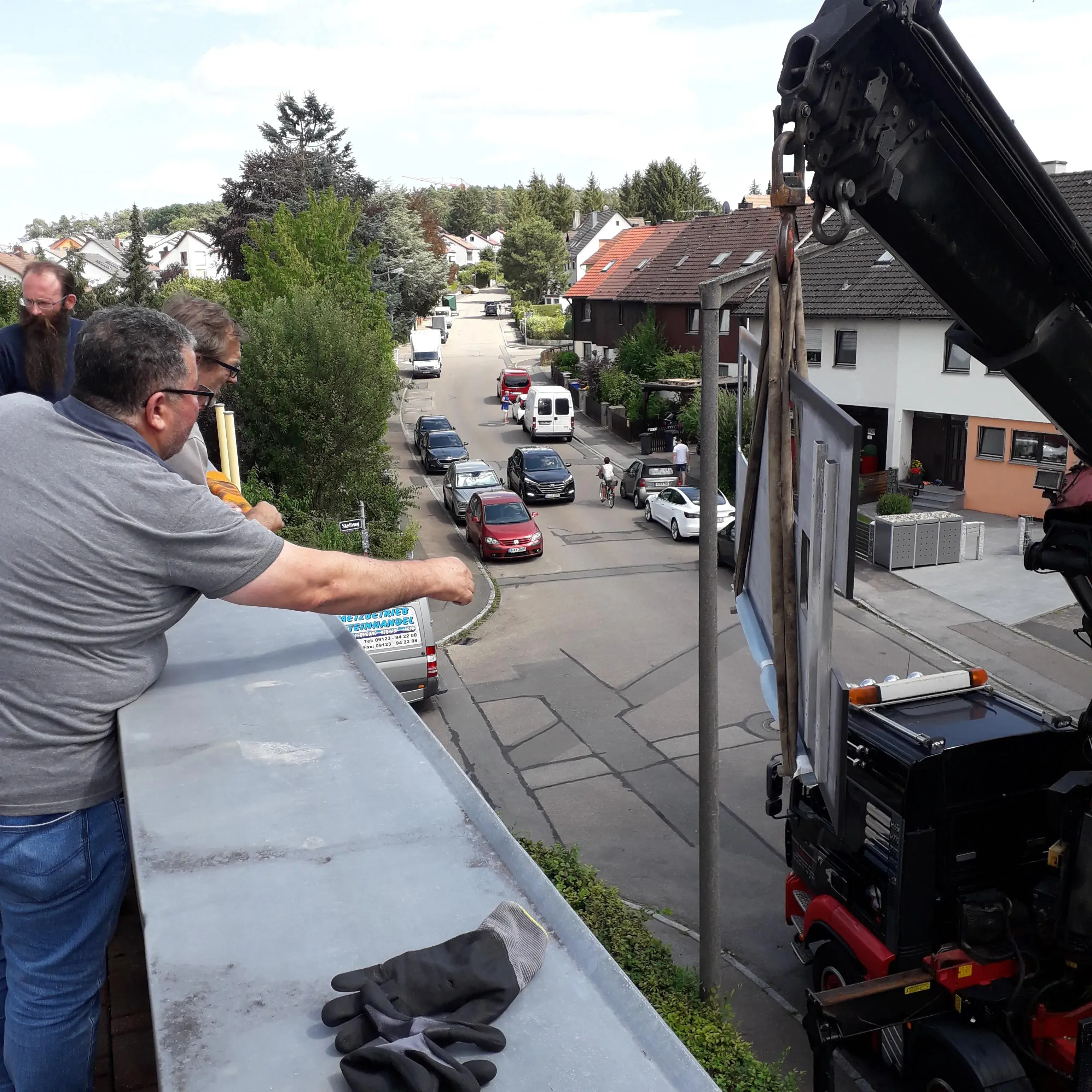 Männer beobachten einen Kran, der ein Objekt auf einen Balkon hebt, Straße mit Autos im Hintergrund.