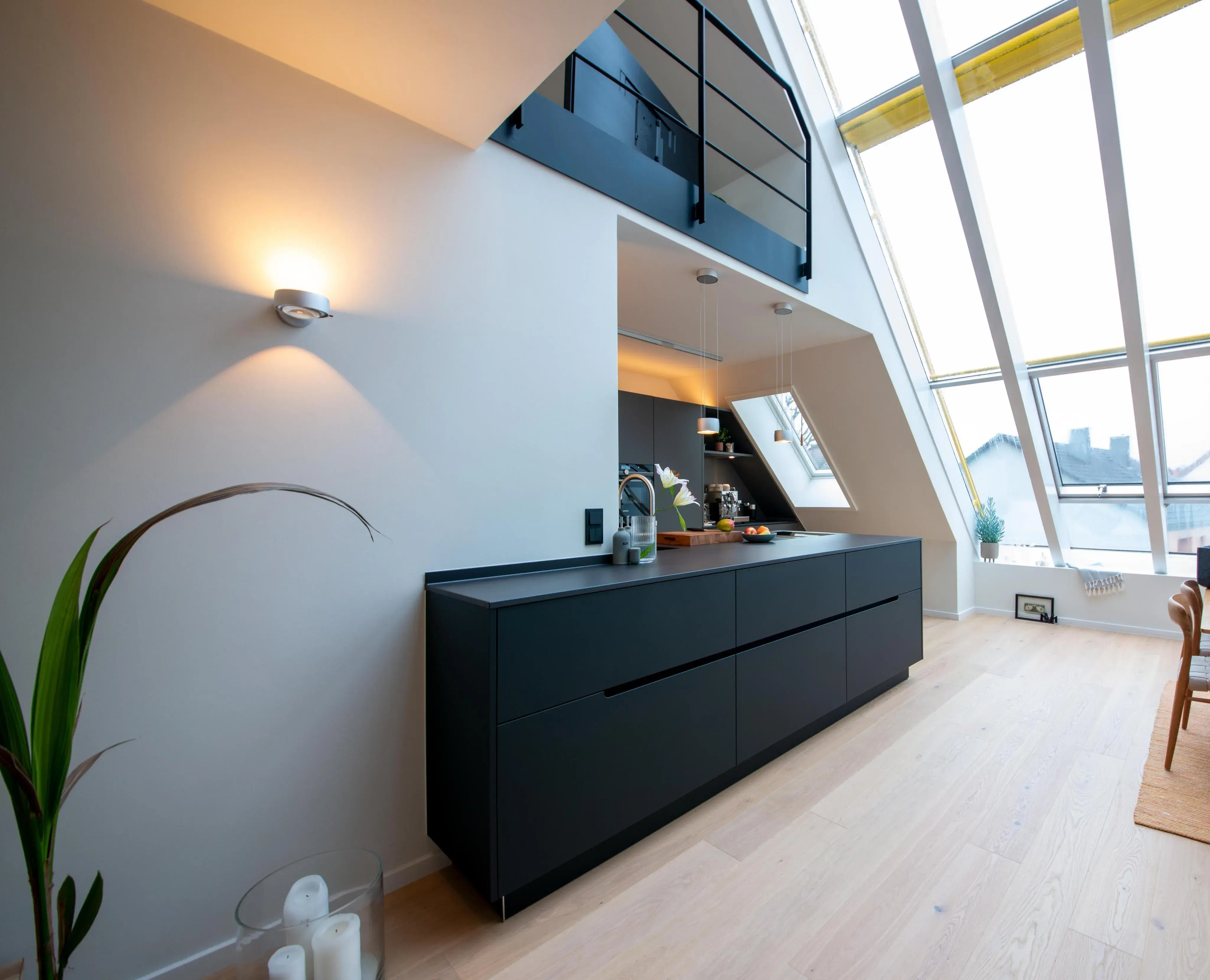 Moderne offene Küche mit schwarzer Einrichtung, viel Tageslicht durch schräge Fenster.