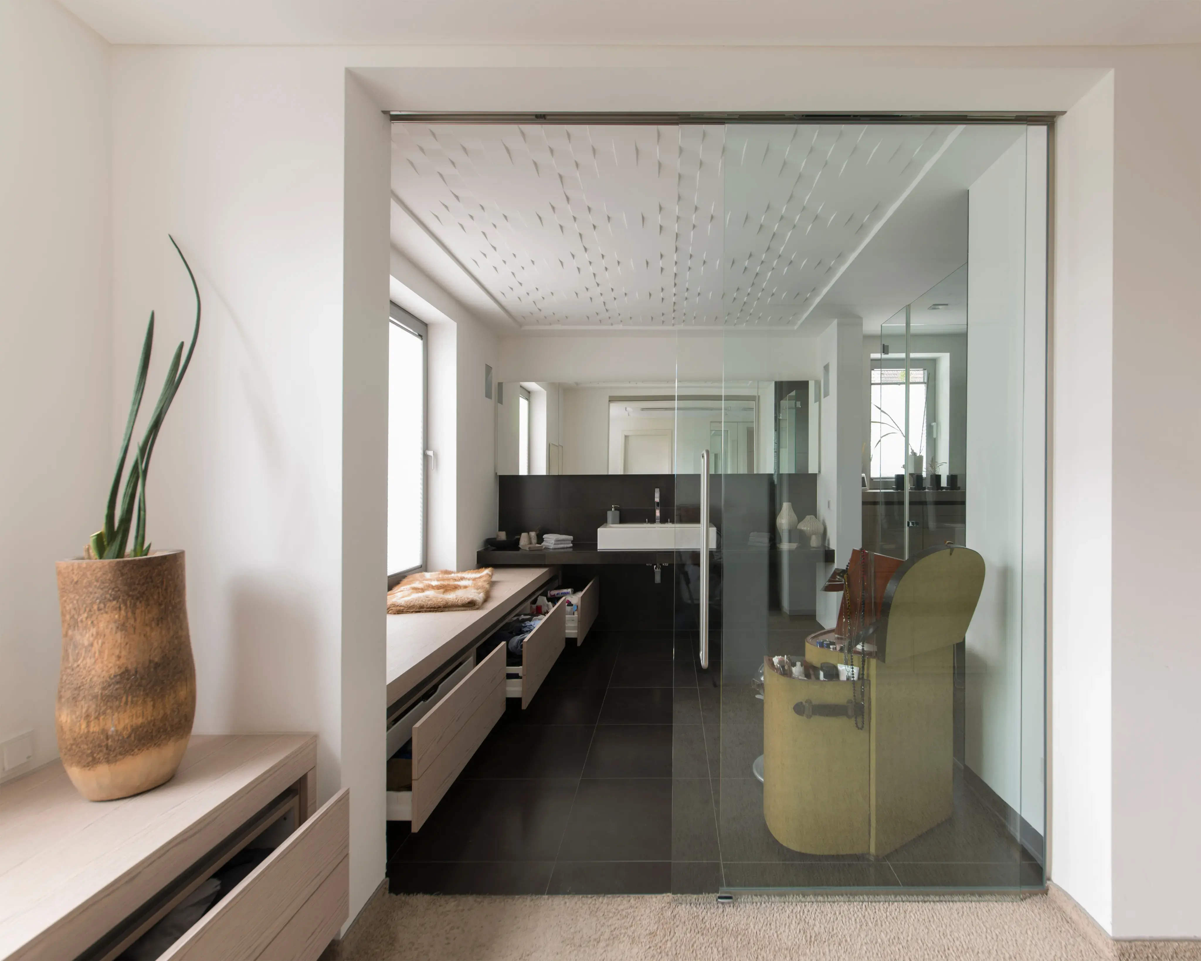 Modernes Badezimmer mit Glaswand, zwei Waschbecken und grünem Sessel.