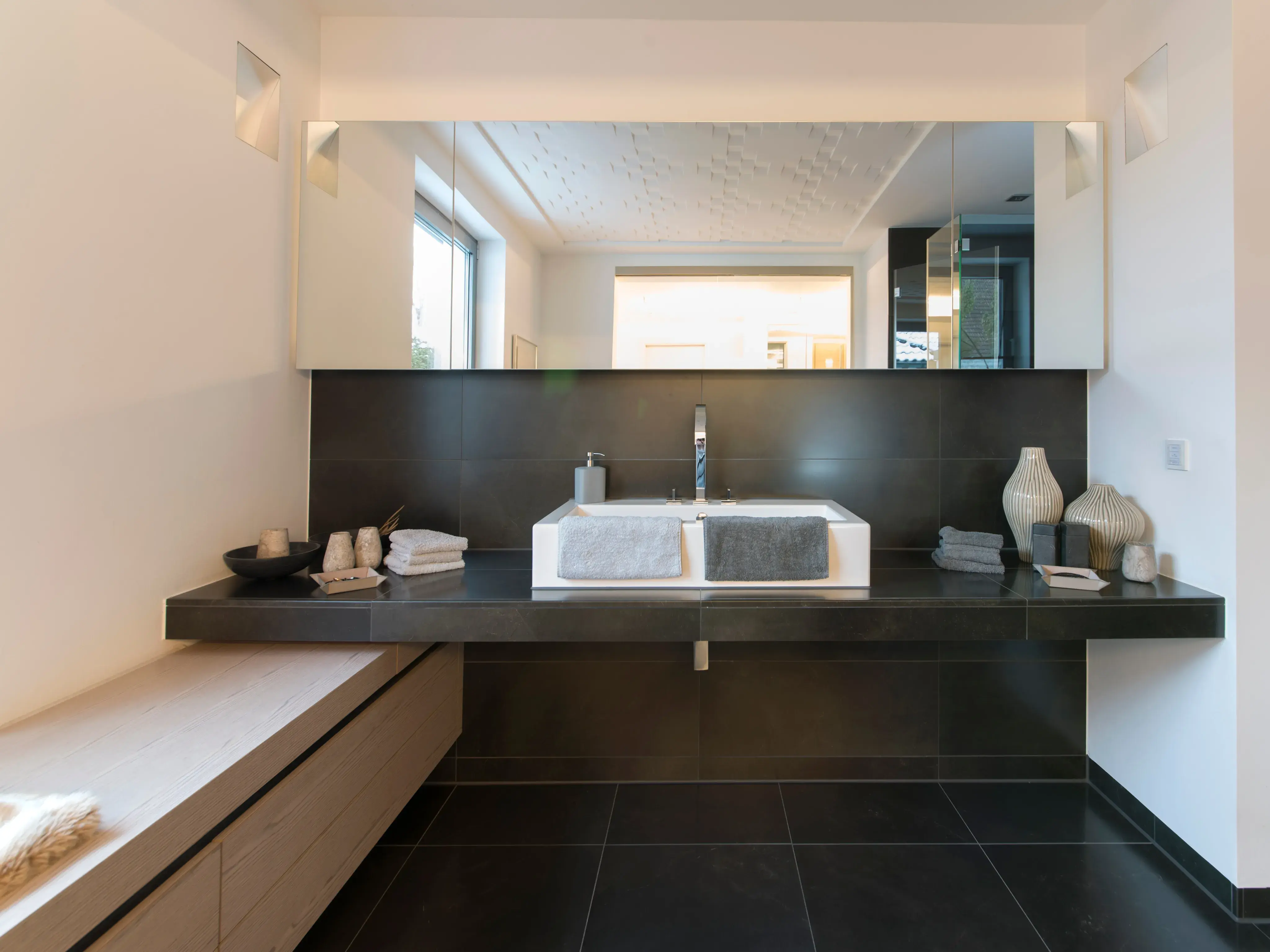 Modernes Badezimmer mit großem Spiegel, schwarzer Ablage und rechteckigem Waschbecken.