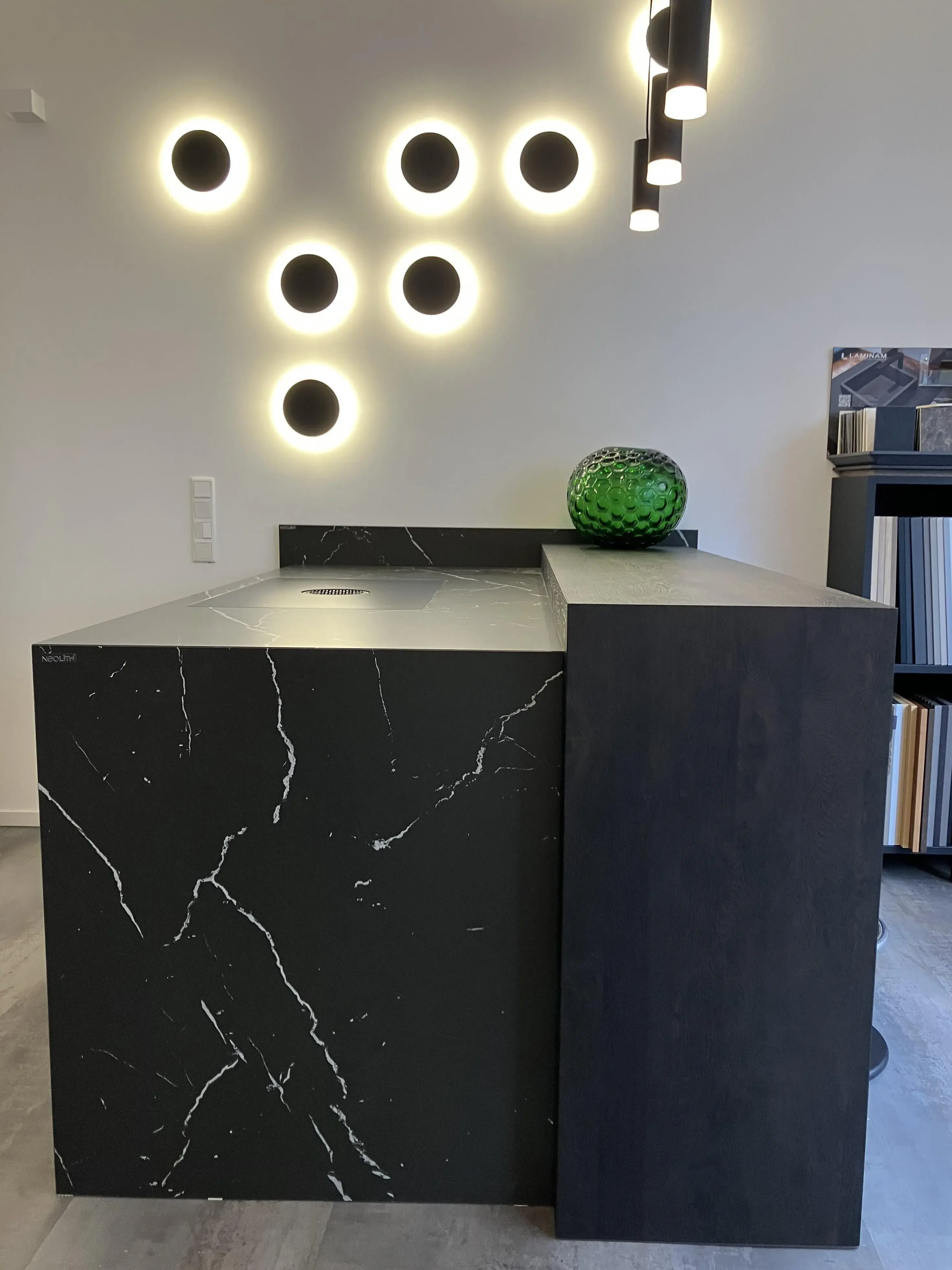 Moderne Küche mit schwarzer Theke, runder Glasvase und leuchtenden Wandkreisen.