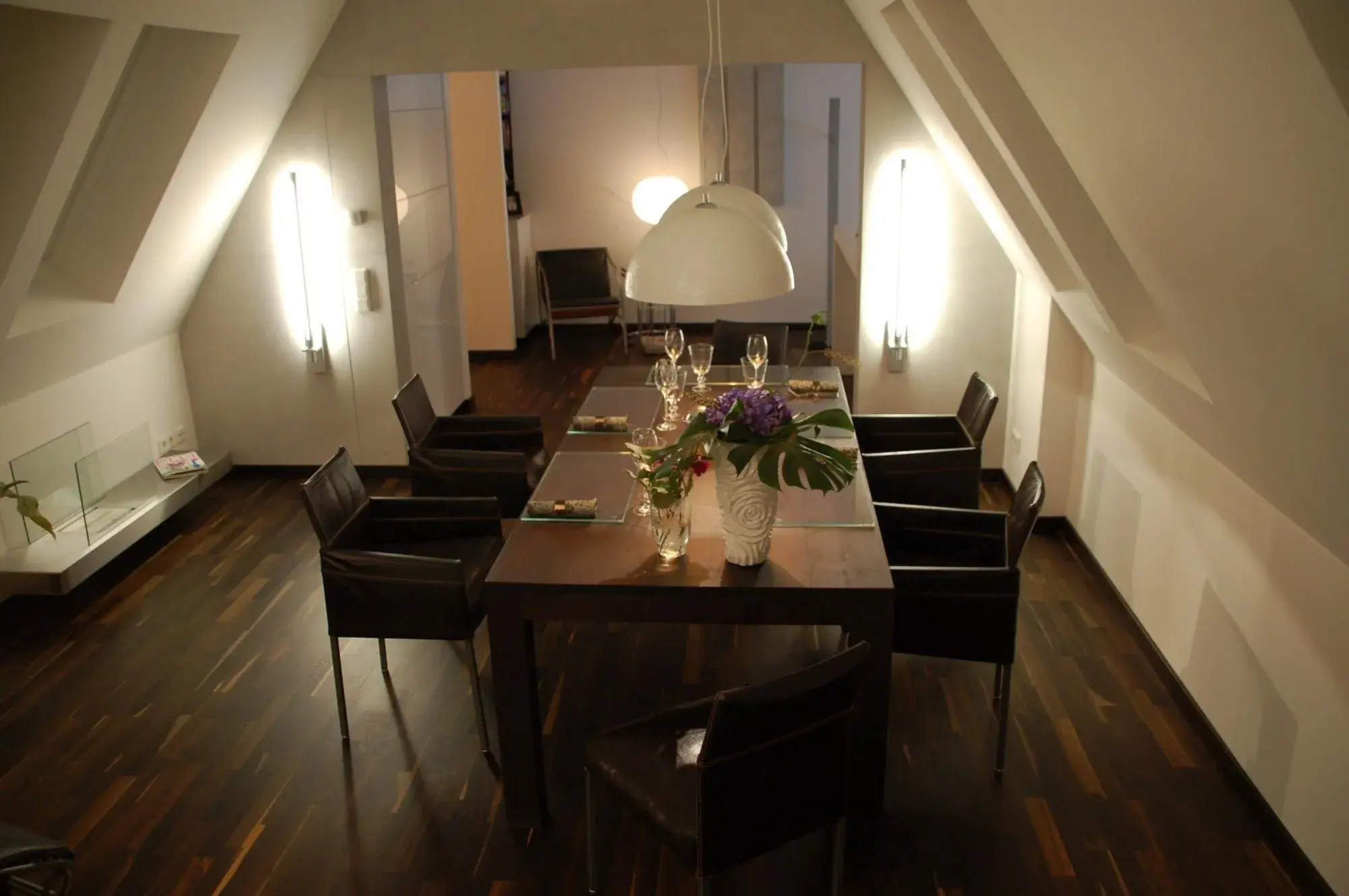 Modernes Esszimmer mit dunklem Holzboden, Tisch, sechs Stühlen und Blumen als Dekoration.