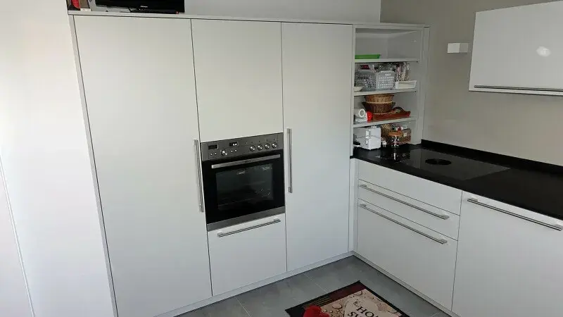 Moderne weiße Küche mit Einbauherd und schwarzer Arbeitsfläche.