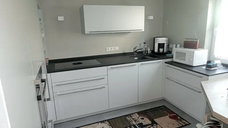 Moderne weiße Küche mit Kaffeemaschine, Mikrowelle und Kochfeld bei Tageslicht.