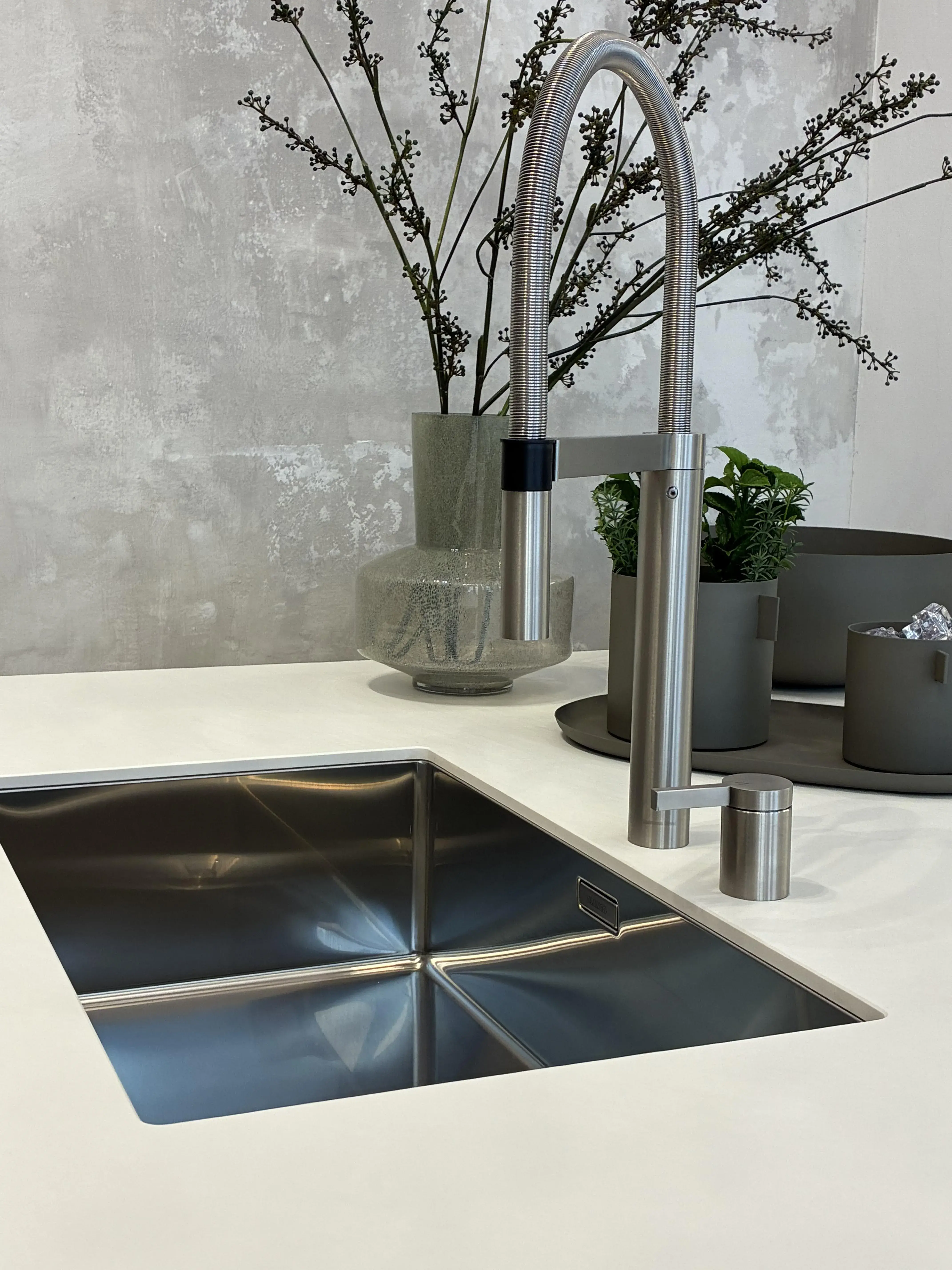 Moderne Küchenspüle mit Wasserhahn, dahinter Vasen mit Zweigen und Pflanzen.
