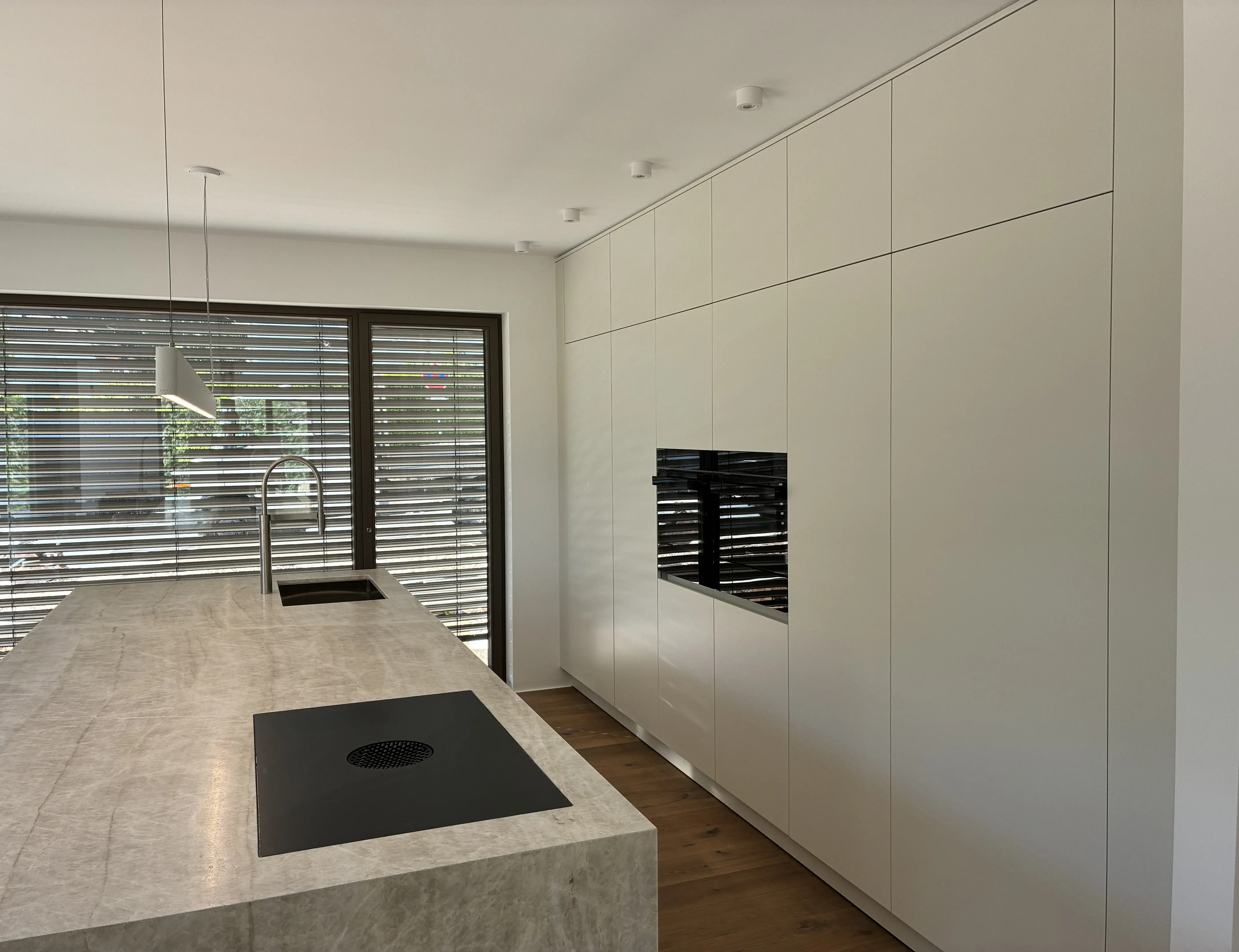 Moderne, helle Küche mit Kochinsel, Einbaugeräten und großen Fensterjalousien.