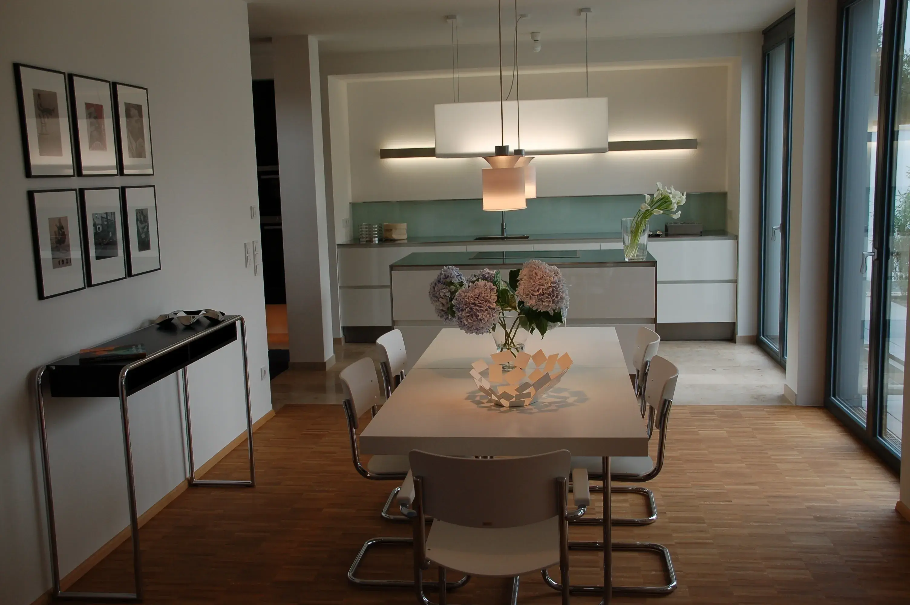 Modernes Esszimmer mit weißen Möbeln, Blumen auf dem Tisch und viel Tageslicht