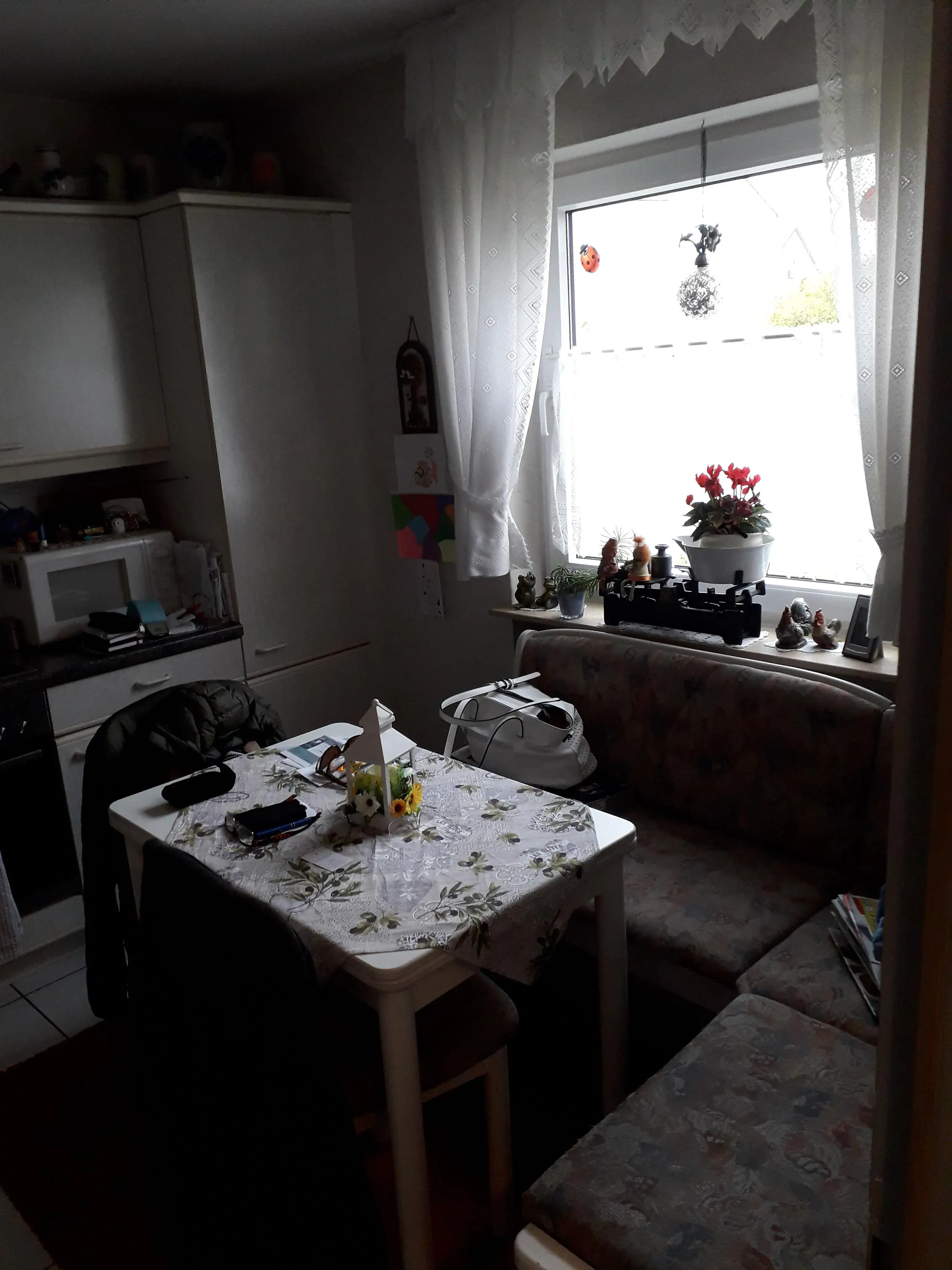 Kleine Küche mit Eckbank, gedecktem Tisch und Fenster mit weißen Gardinen.