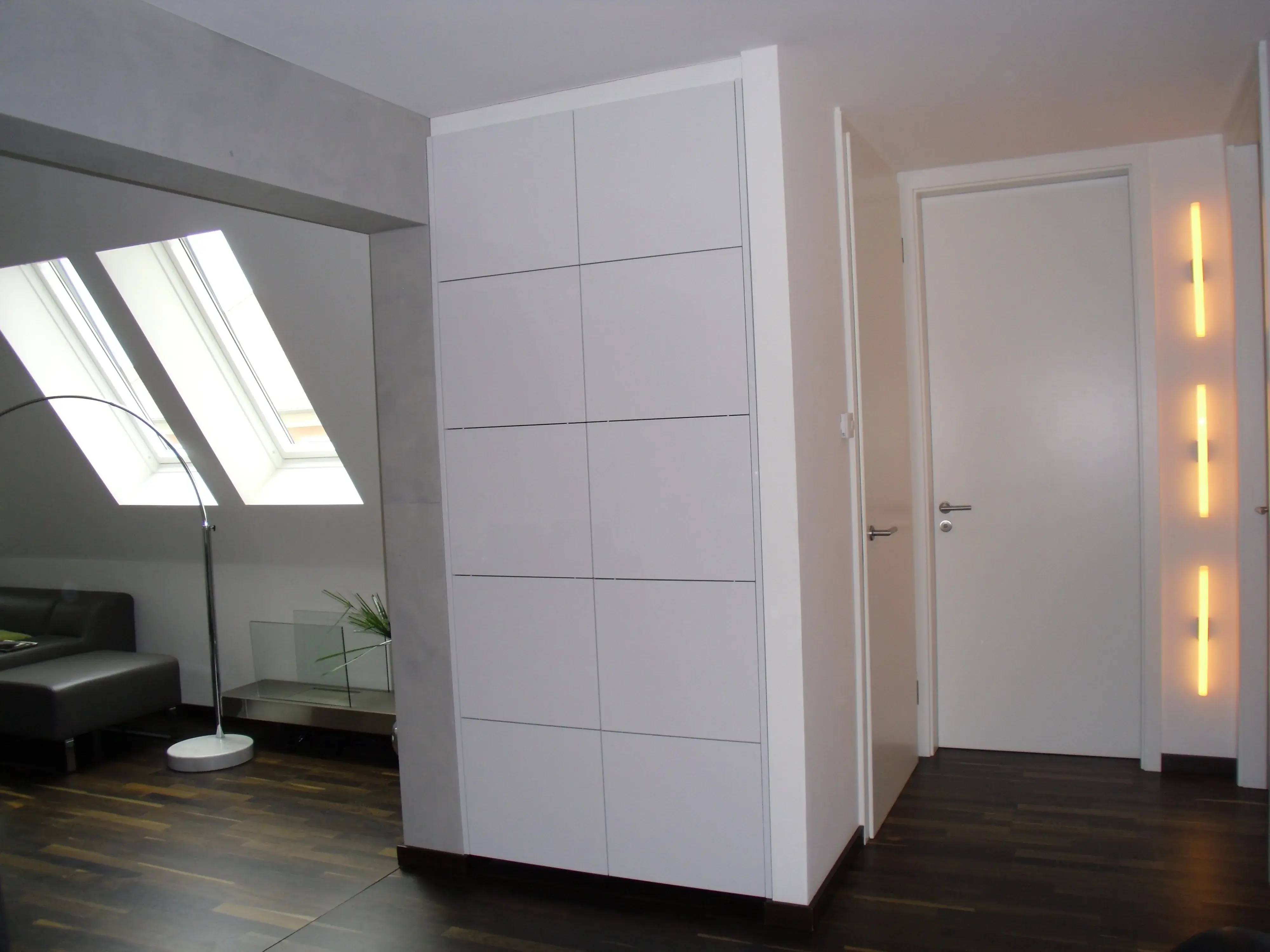 Modernes, helles Zimmer mit Dachfenstern, dunklem Holzboden und weißer Tür.