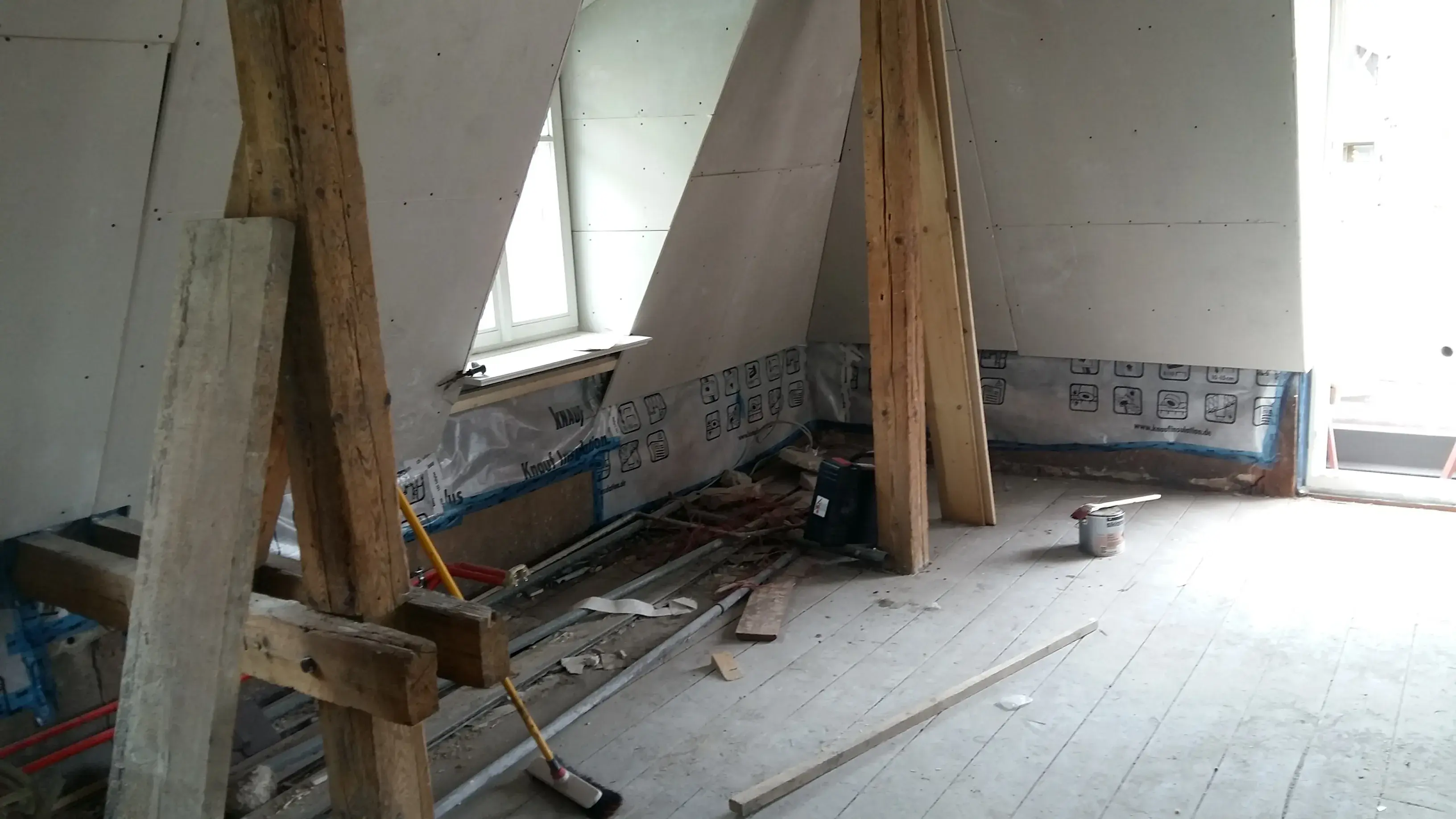Dachgeschoss im Umbau mit sichtbaren Balken und Baumaterialien auf dem Boden.